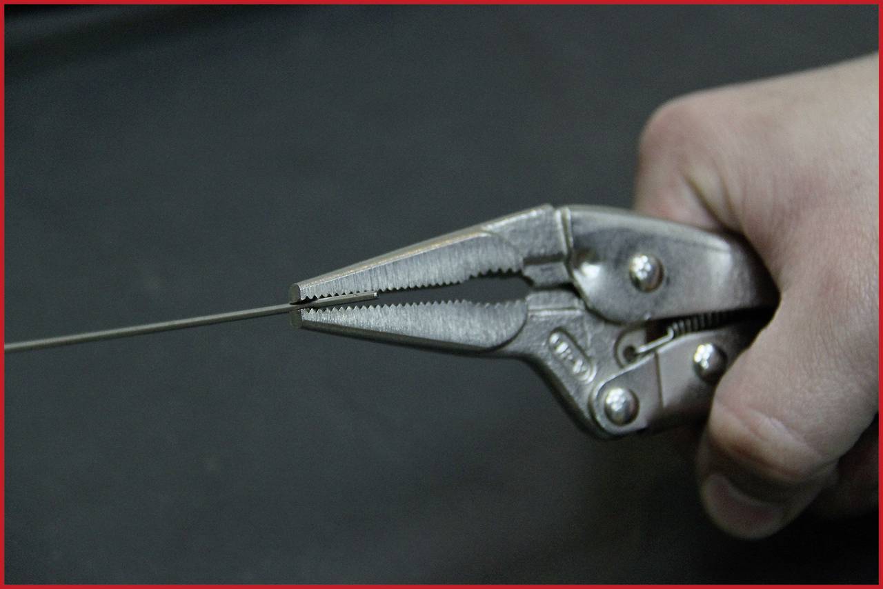 Eine Hand hält eine verstellbare Zange, die fest einen dünnen Metalldraht umklammert.