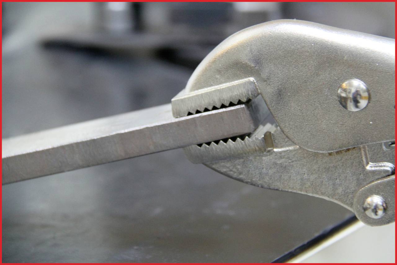 Eine Metallzange hält fest ein Metallstück auf einer grauen Oberfläche.