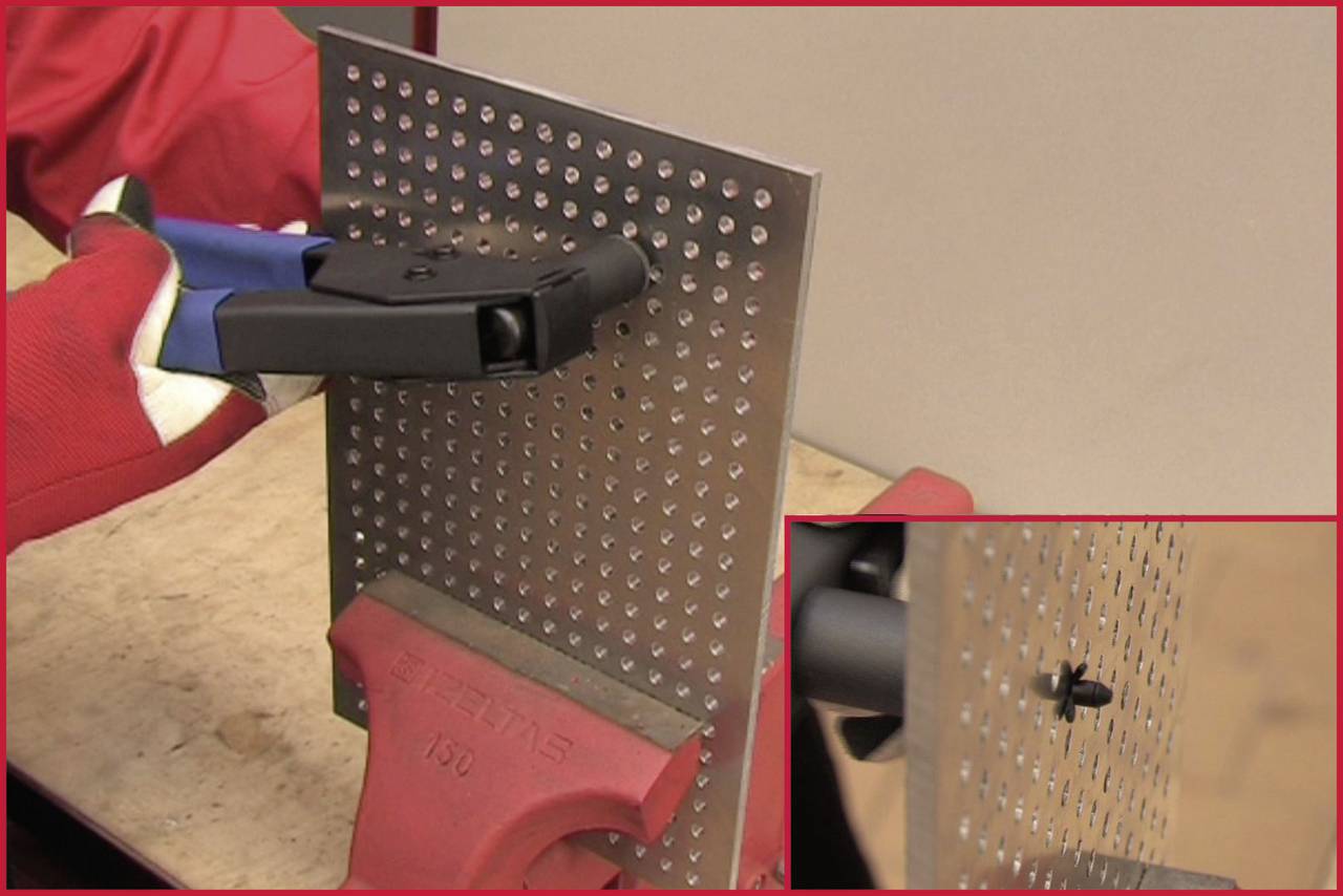 Eine Person in roten Handschuhen verwendet ein Werkzeug, um eine Blindniete in ein perforiertes Metallblech einzusetzen, das in einem Schraubstock fixiert ist.