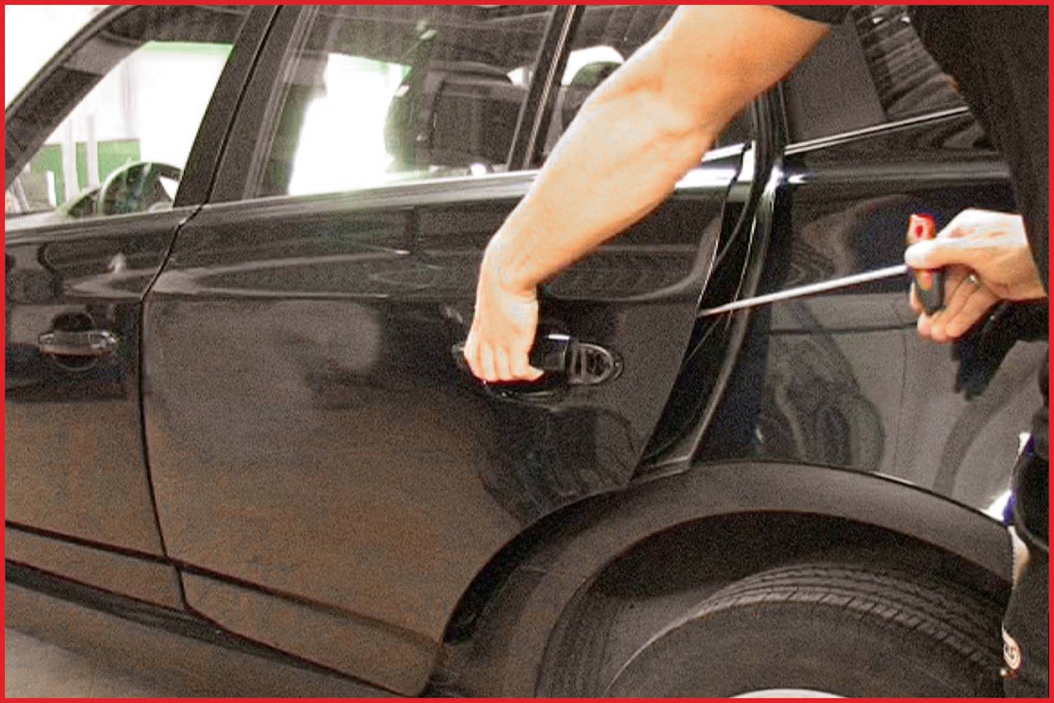 Eine Person versucht, die Tür eines schwarzen Autos mit einem Schraubendreher gewaltsam zu öffnen.
