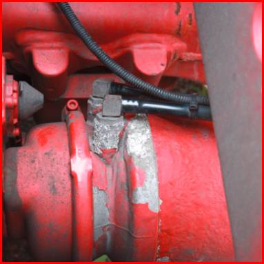 Ein rotes mechanisches Teil mit Kabel und Verschraubung, möglicherweise ein Teil eines Motors oder einer Maschine, teilweise abgenutzt.