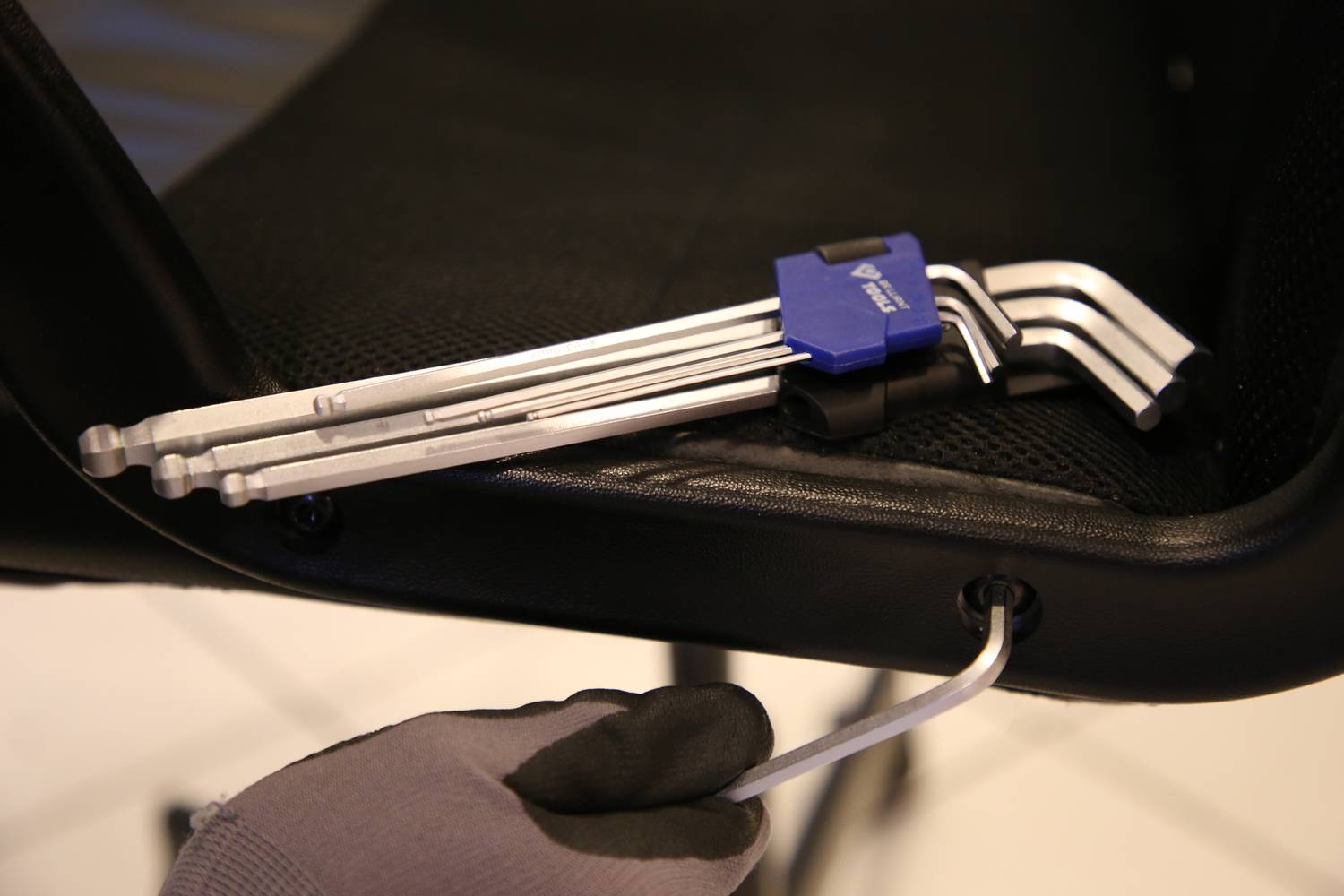 Person montiert mit Inbusschlüssel einen Stuhl. Ein Bündel weiterer Inbusschlüssel liegt auf der Stuhlfläche.