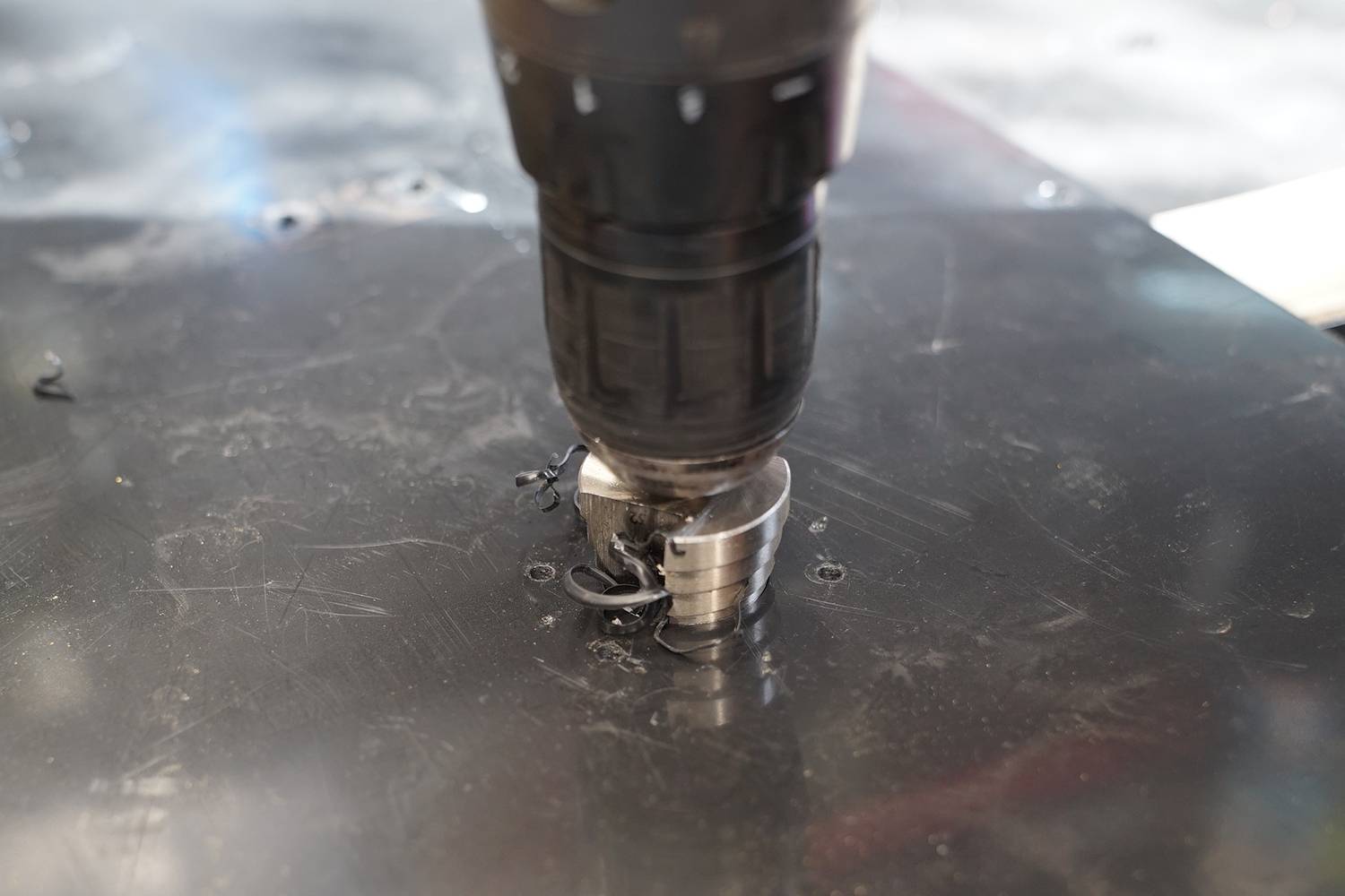 Bohrmaschine bohrt ein Loch in ein schwarzes Metallstück, Metallspäne um das Loch herum.