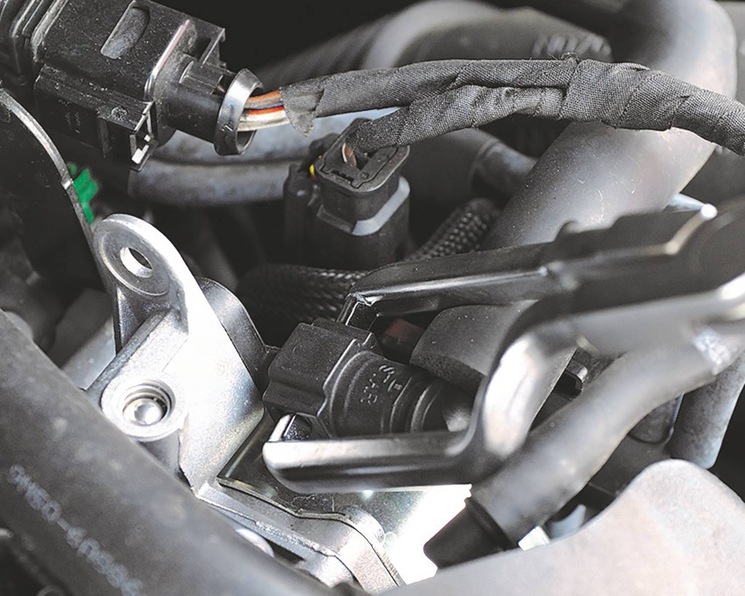 Nahaufnahme eines Motorteils mit mehreren Kabelverbindungen und Metallkomponenten. Zeigt die Komplexität der Automobiltechnik.