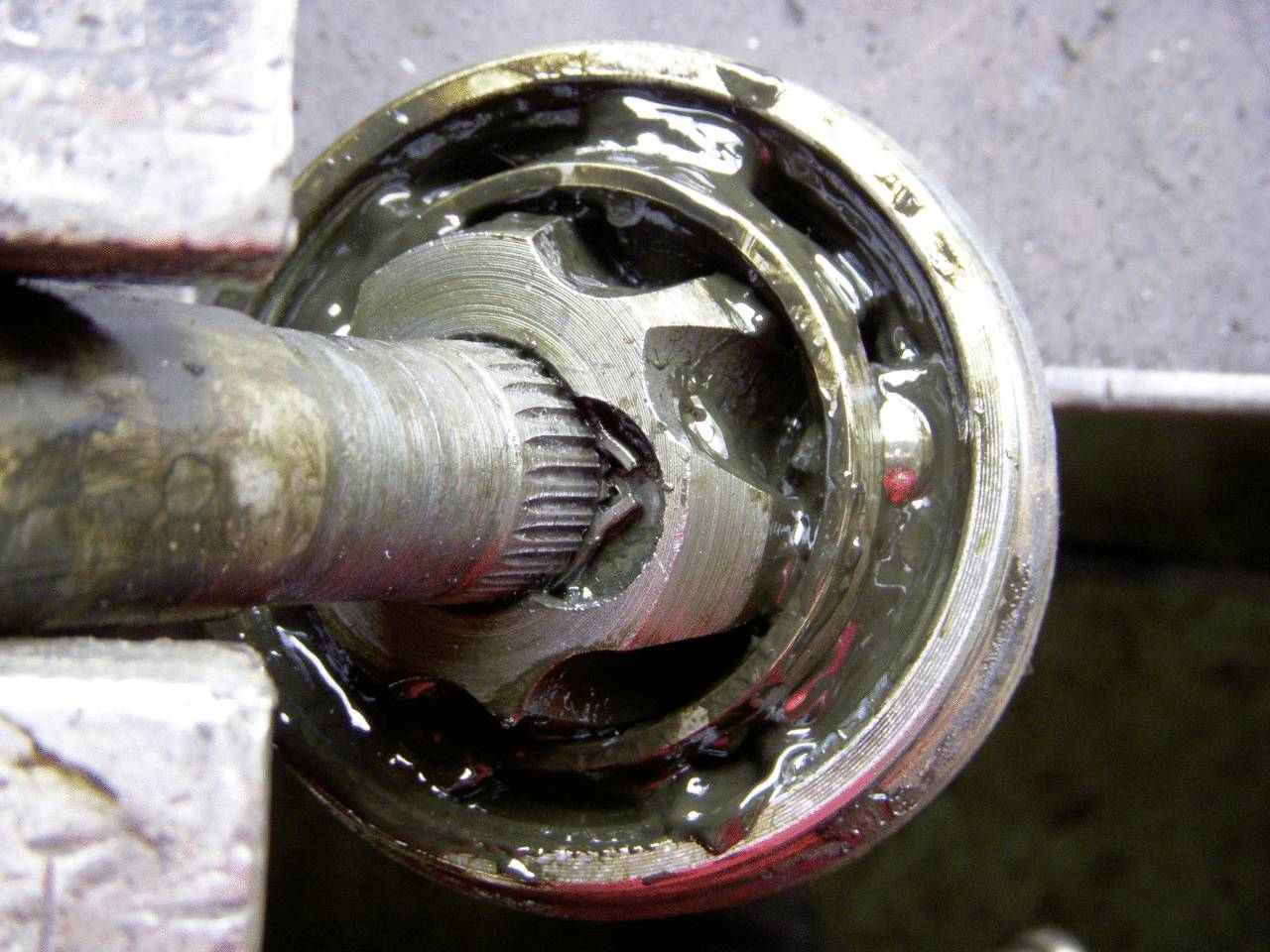 Nahaufnahme eines beschädigten Gelenks mit Austritt von Schmiermittel. Fokus auf die Metallverzahnung und den umliegenden Mechanismus.