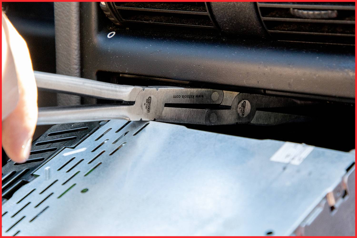 Eine Hand benutzt ein spezielles Werkzeug, um ein Autoradio aus einem Armaturenbrett zu entfernen.