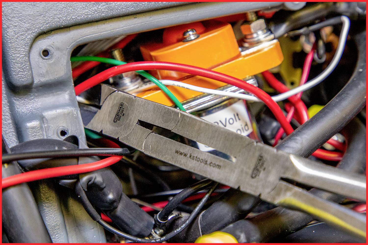 Blick auf eine elektrische Verkabelung in einem Gerät mit farbigen Kabeln, einer orangenen Komponente und einer Zange im Vordergrund.