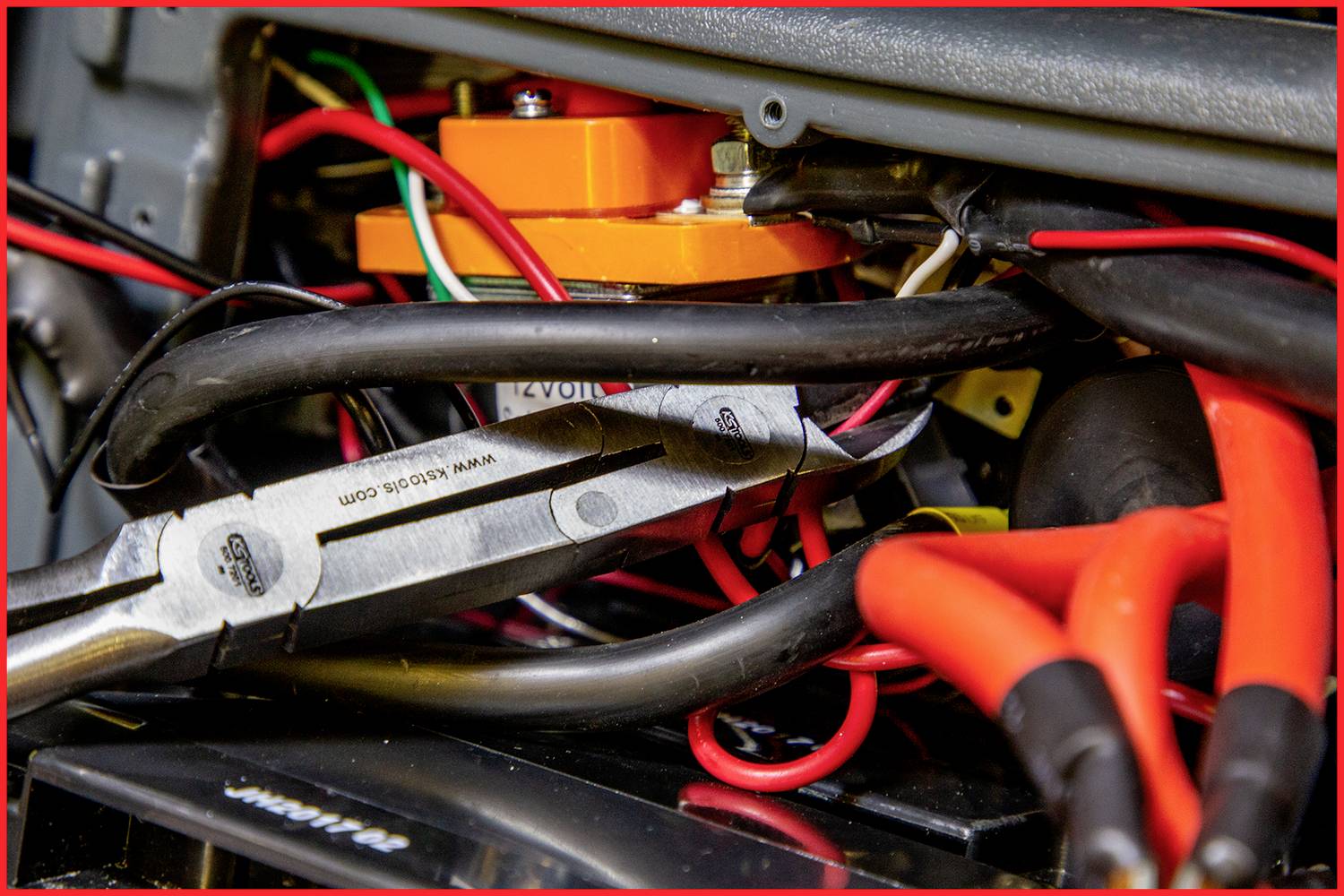 Werkzeuge und Kabel in engem Raum; Nahaufnahme von isolierten Drähten, Zangen und Schrauben, die an einem elektrischen Gerät arbeiten.