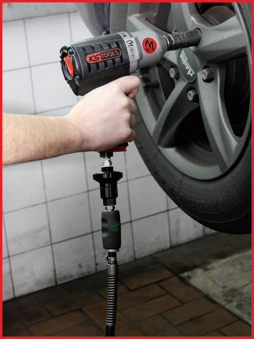 Eine Person befestigt ein Autoreifen mit einem Schlagschrauber in einer Werkstatt. Der Reifen ist auf einer Hebebühne montiert.