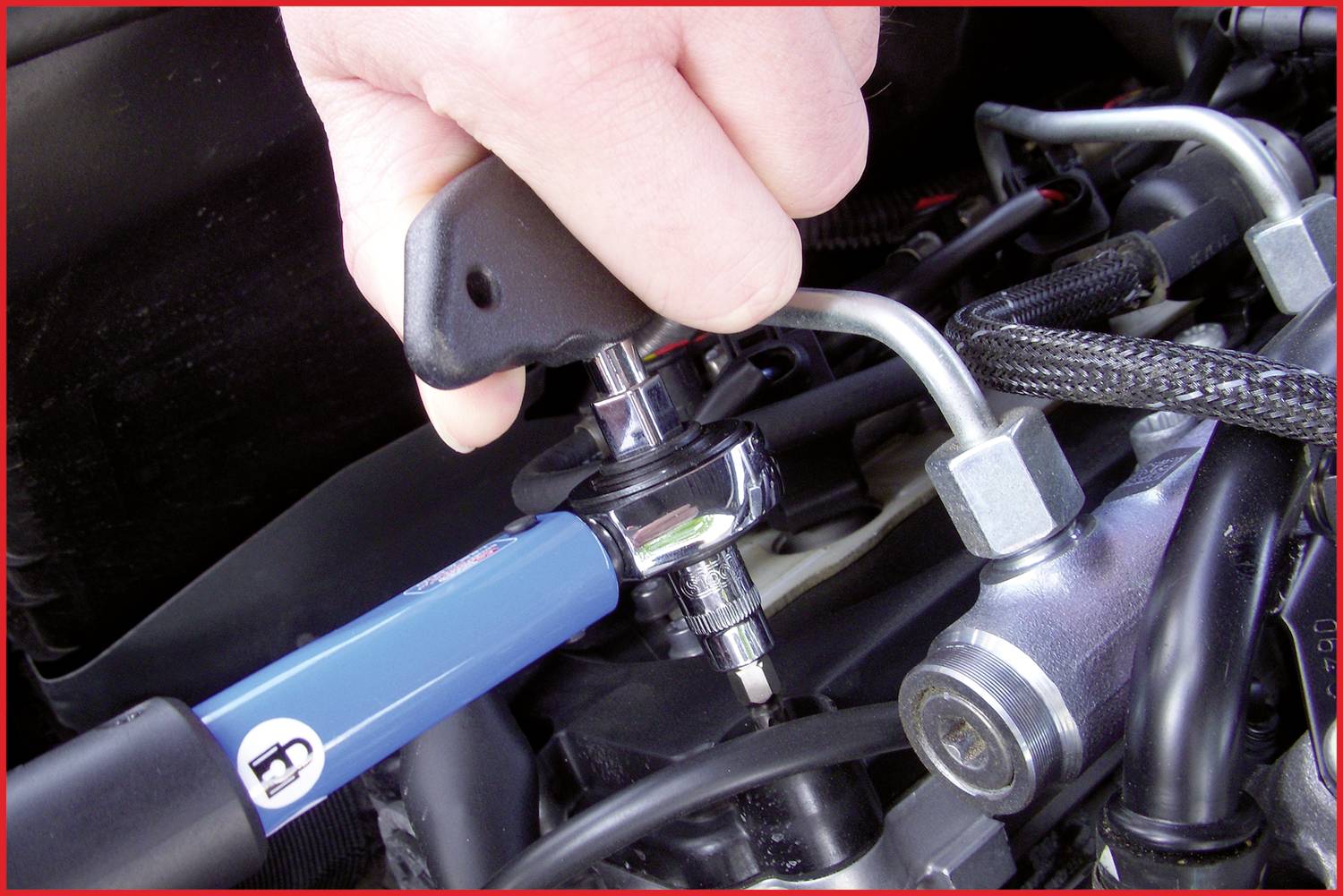 Hand zieht mit einem Drehmomentschlüssel eine Schraube an einem Motor an. Kabel und Schläuche sichtbar. Fokus auf korrekte Anwendung von Werkzeugen.