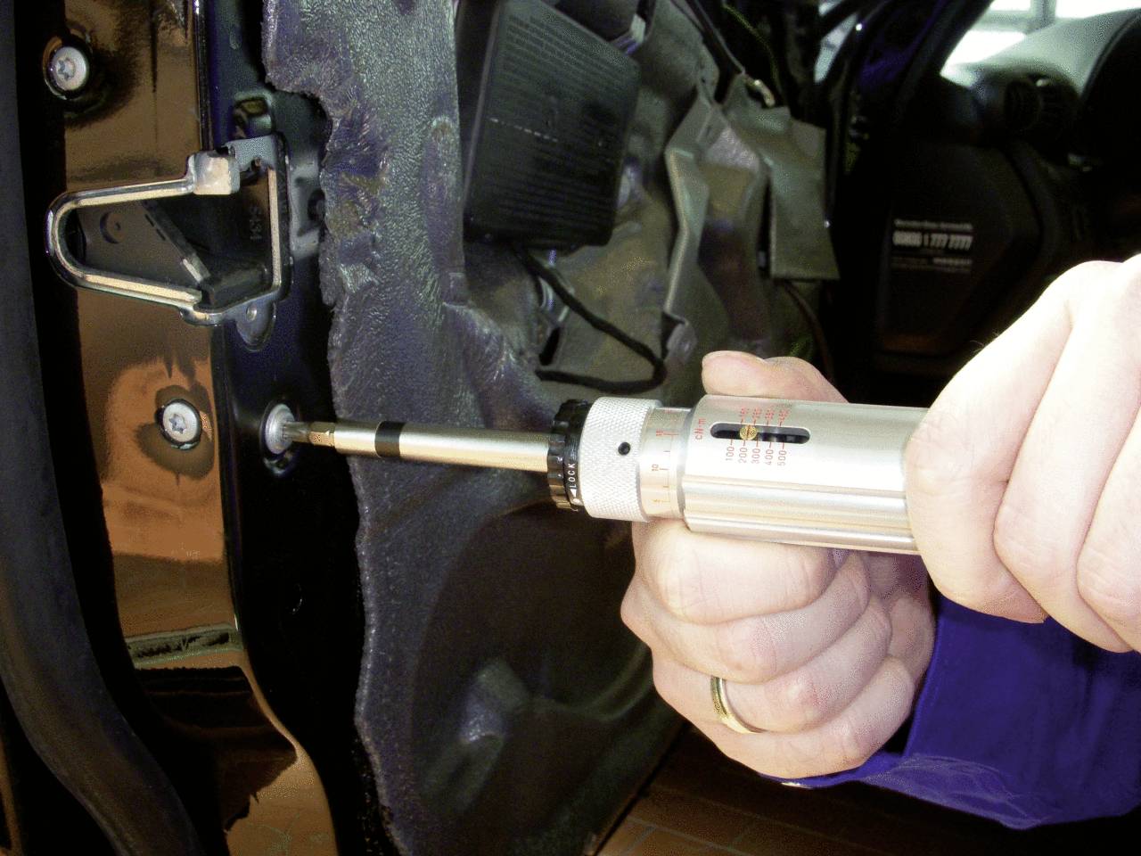 Eine Hand hält einen Schraubendreher und zieht eine Schraube an einer Autotür an, vermutlich bei der Reparatur oder Montage.