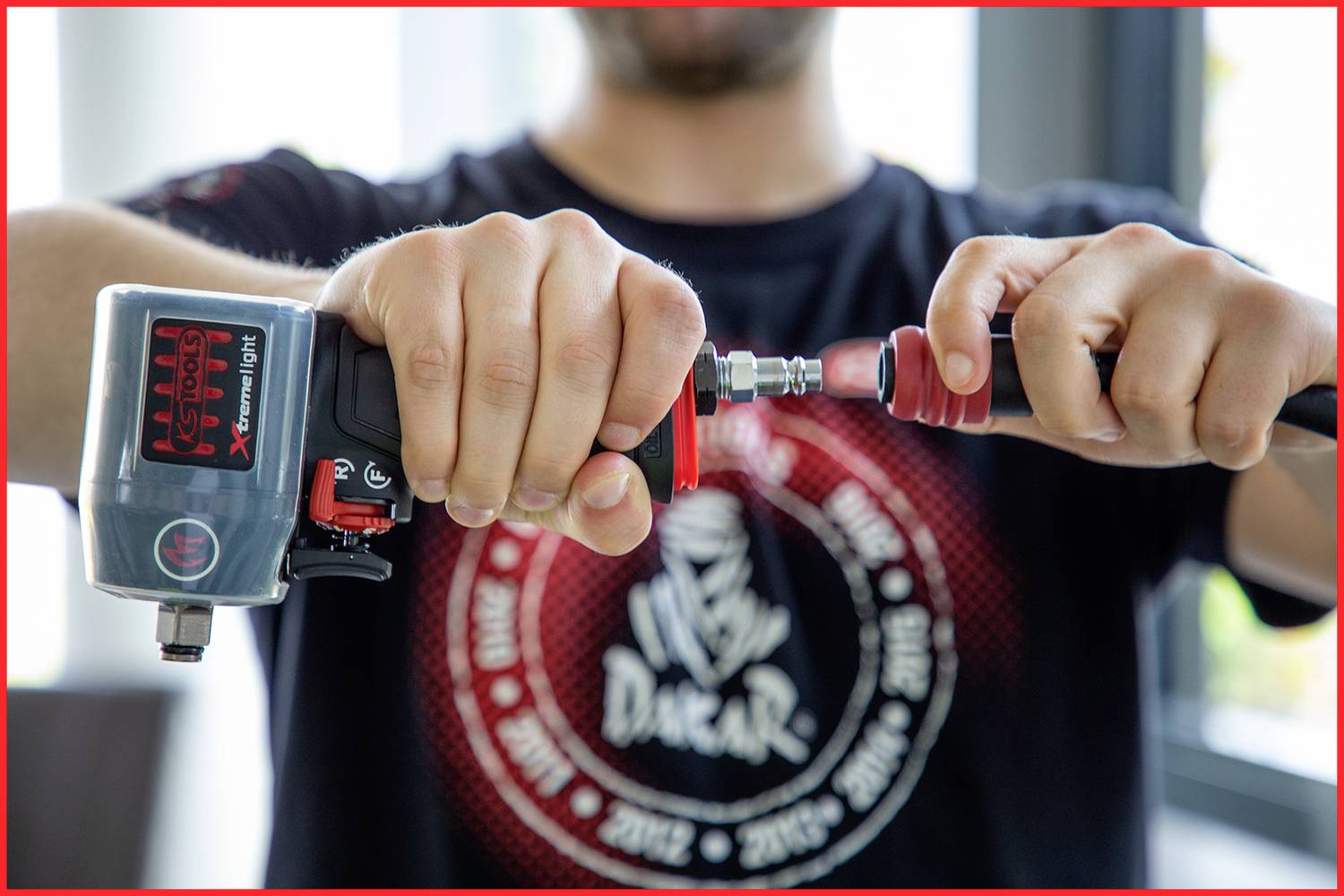 Eine Person hält ein Pneumatikwerkzeug in beiden Händen, bereitet es für den Gebrauch vor. Der Motor ist im Hintergrund verschwommen.