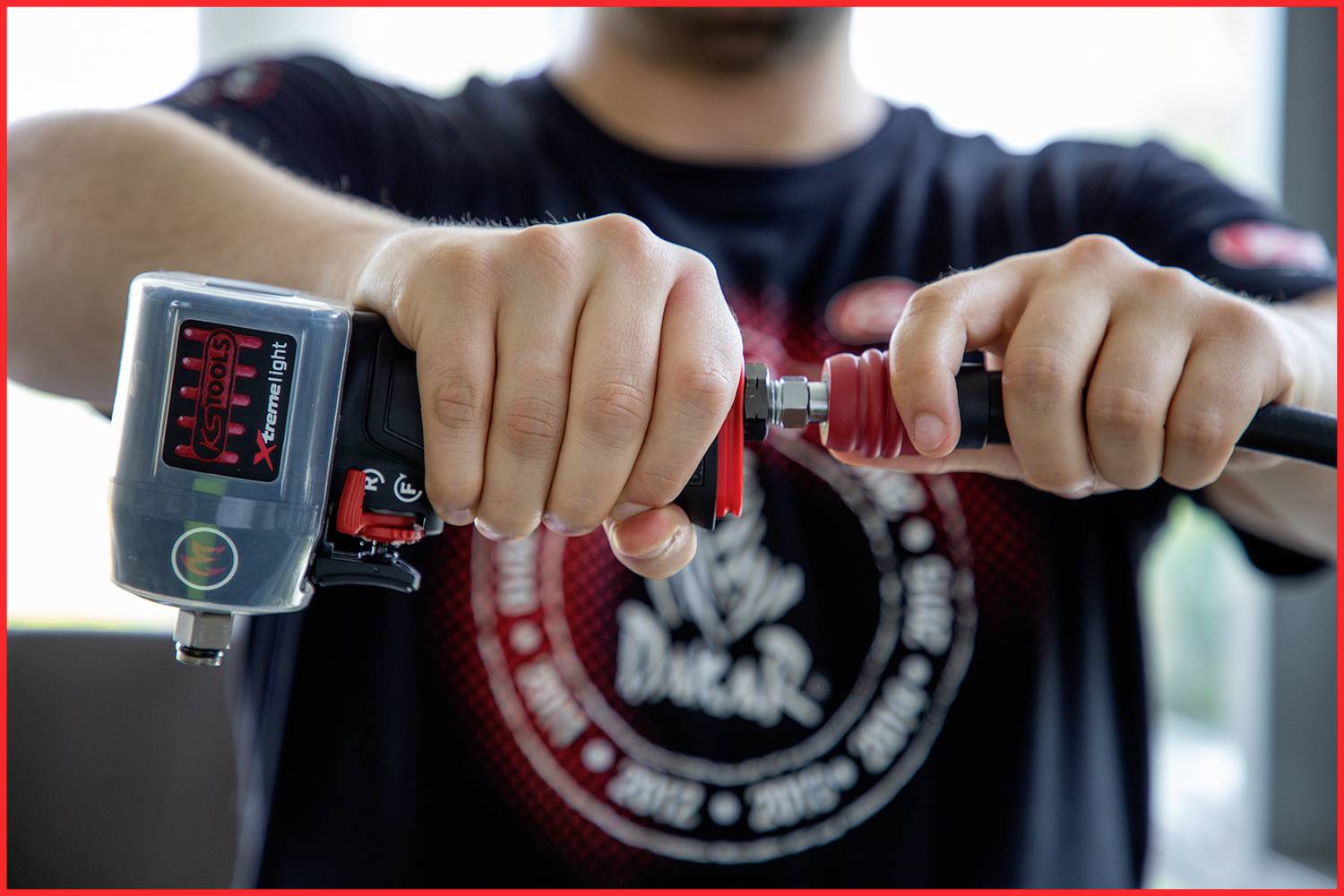 Eine Person verbindet einen Druckluftschlauch mit einem Werkzeug in einer Werkstatt, Fokus auf den Händen und dem Anschluss.