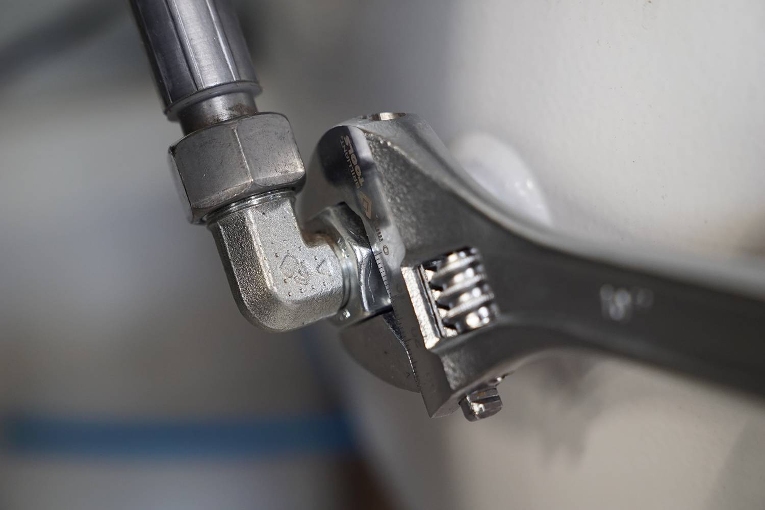 Ein Schraubenschlüssel zieht eine Metallverbindung an einem Rohr fest. Nahaufnahme der Handwerkerarbeit mit Fokus auf das Werkzeug.