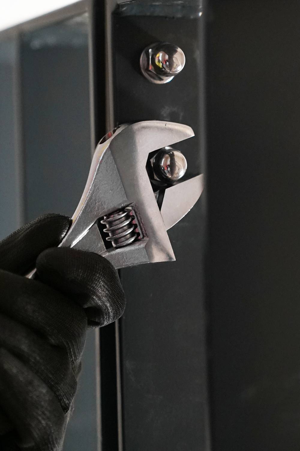 Eine Person in schwarzen Handschuhen verwendet einen verstellbaren Schraubenschlüssel, um eine Schraube an einem Metallrahmen festzuziehen.