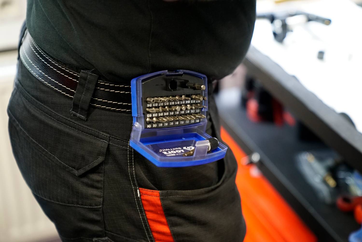 Eine Person trägt ein offenes Etui mit Schraubendreherspitzen an ihrem Gürtel in einer Werkstattumgebung.