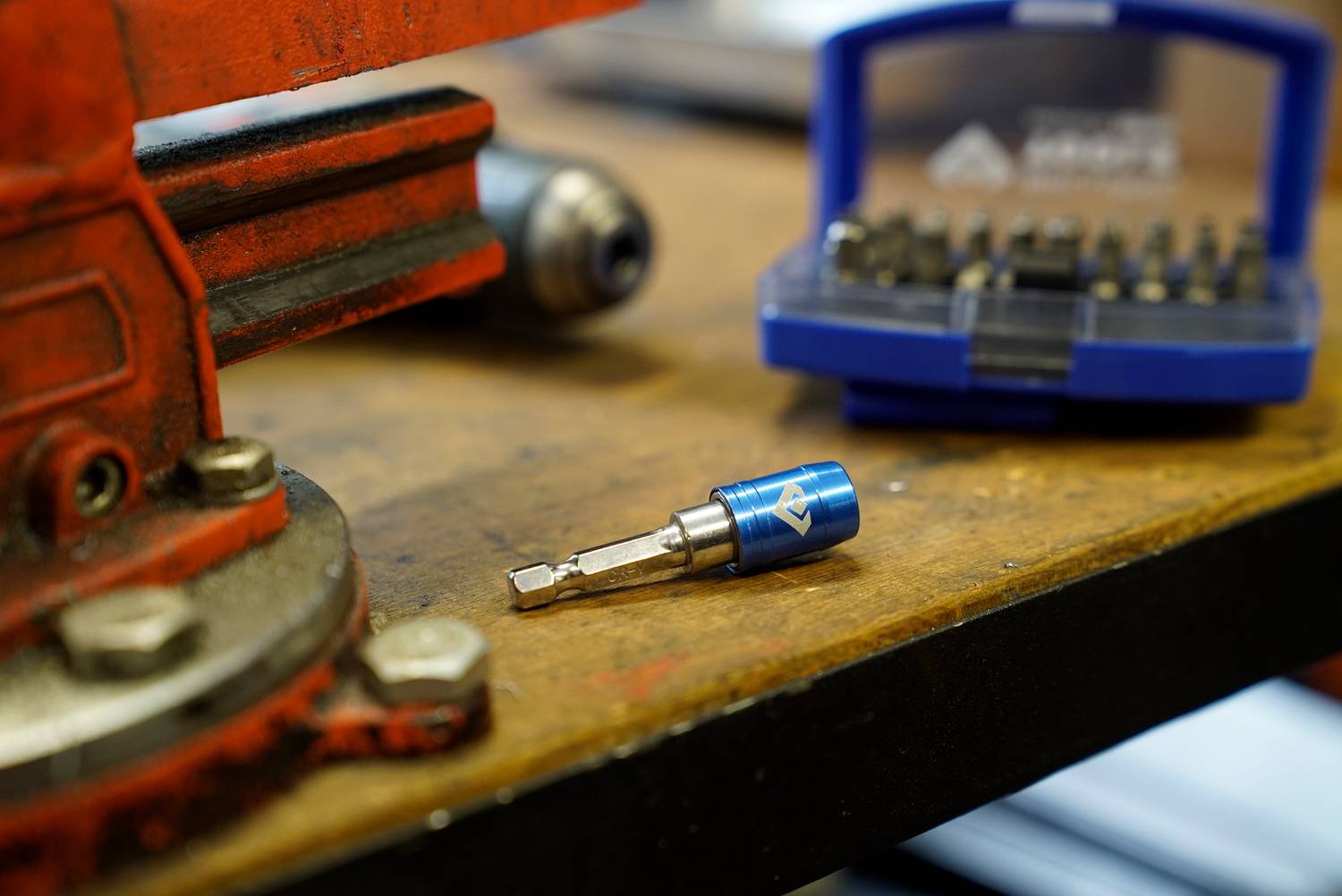 Ein blauer Schraubendreher-Bit liegt auf einer Werkbank, umgeben von einem Schraubstock und einer Bit-Box im Hintergrund.