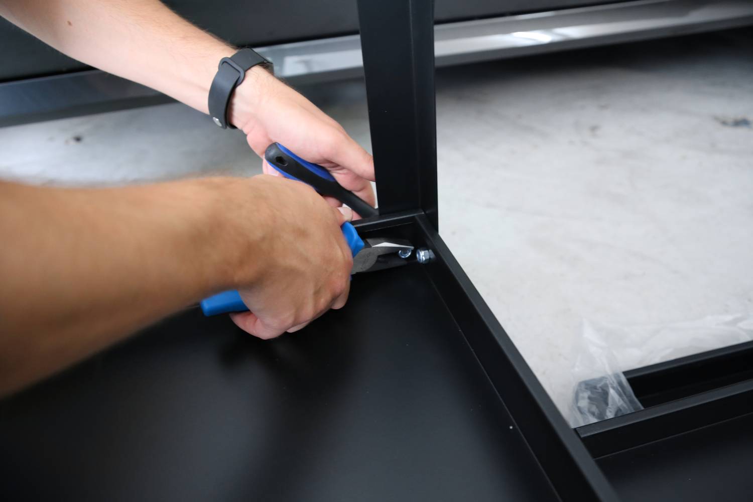 Eine Person montiert mit einem Schraubenschlüssel ein schwarzes Möbelstück.