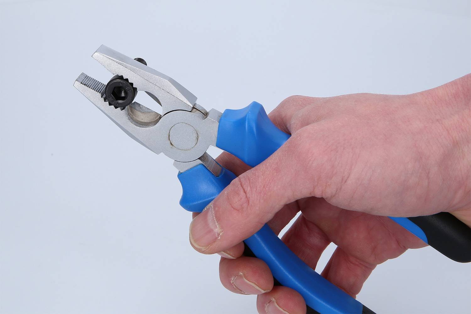 Eine Hand hält eine Zange mit blauem Griff und silbernen Backen, die ein kleines schwarzes Zahnrad greifen.