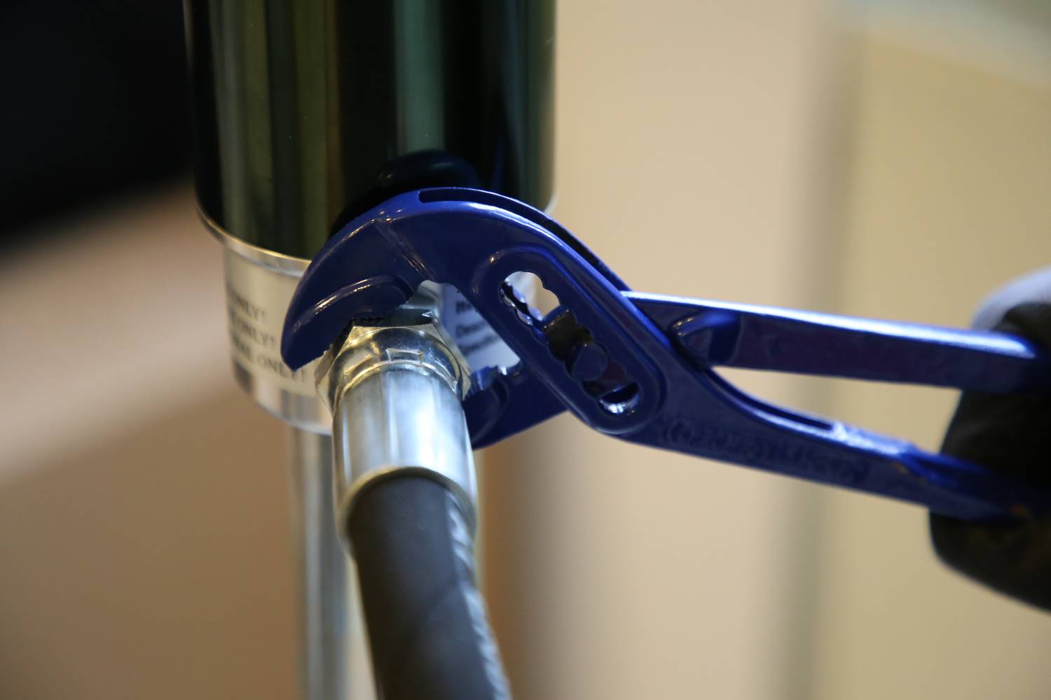 Ein Klempner zieht mit einer blauen Rohrzange an einer Rohrverbindung in einem Inneraum, um sie zu befestigen oder zu lösen.