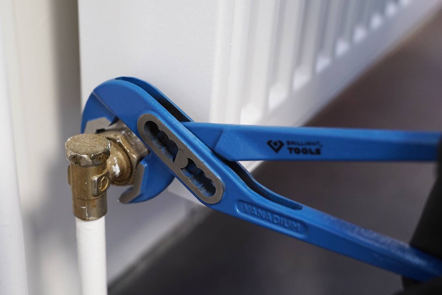 Blaue, verstellbare Rohrzange justiert eine Metallverbindung an einem Heizkörper. Werkzeug in Gebrauch für Installationszwecke.