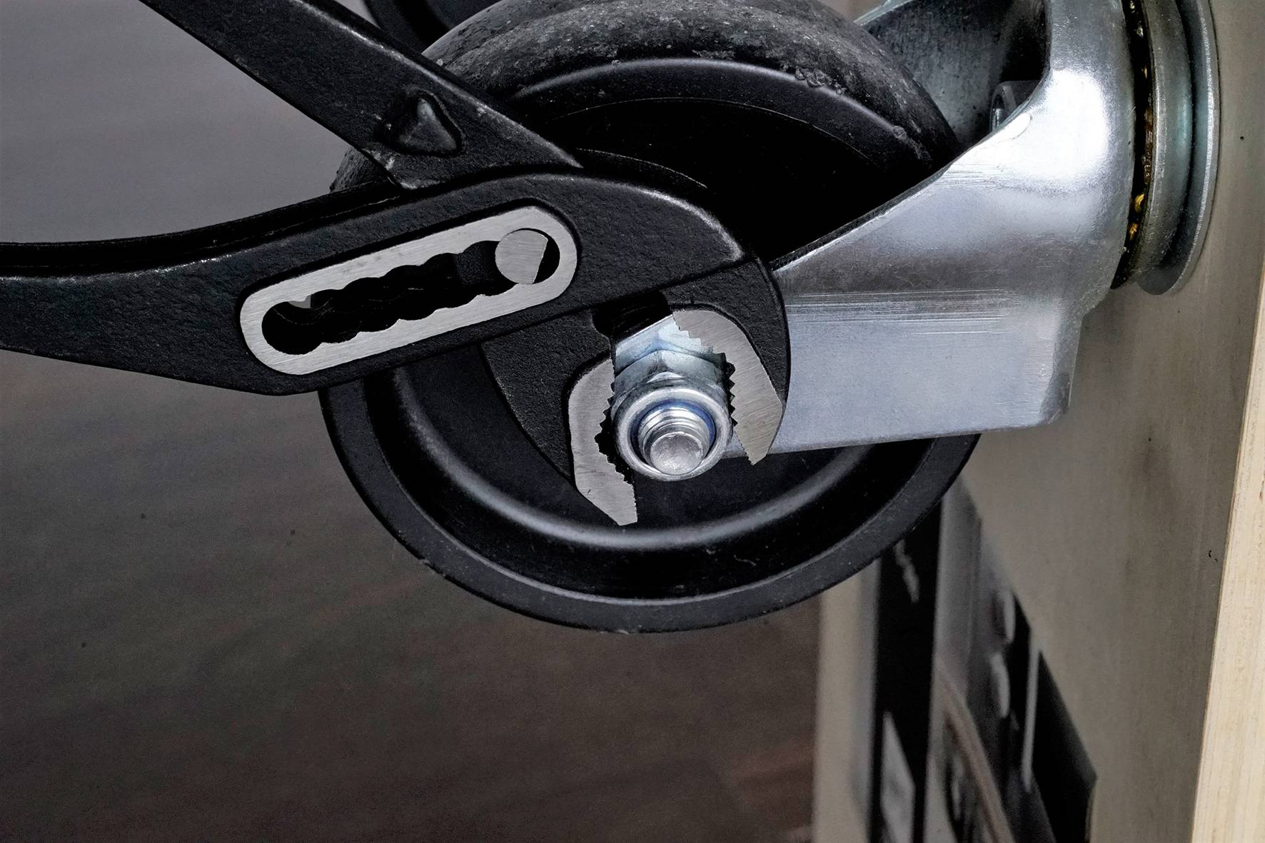 Nahaufnahme eines schwarzen Rades mit einem Schraubenschlüssel, der an einer Mutter ansetzt. Werkzeugarbeit an einem Möbelstück.