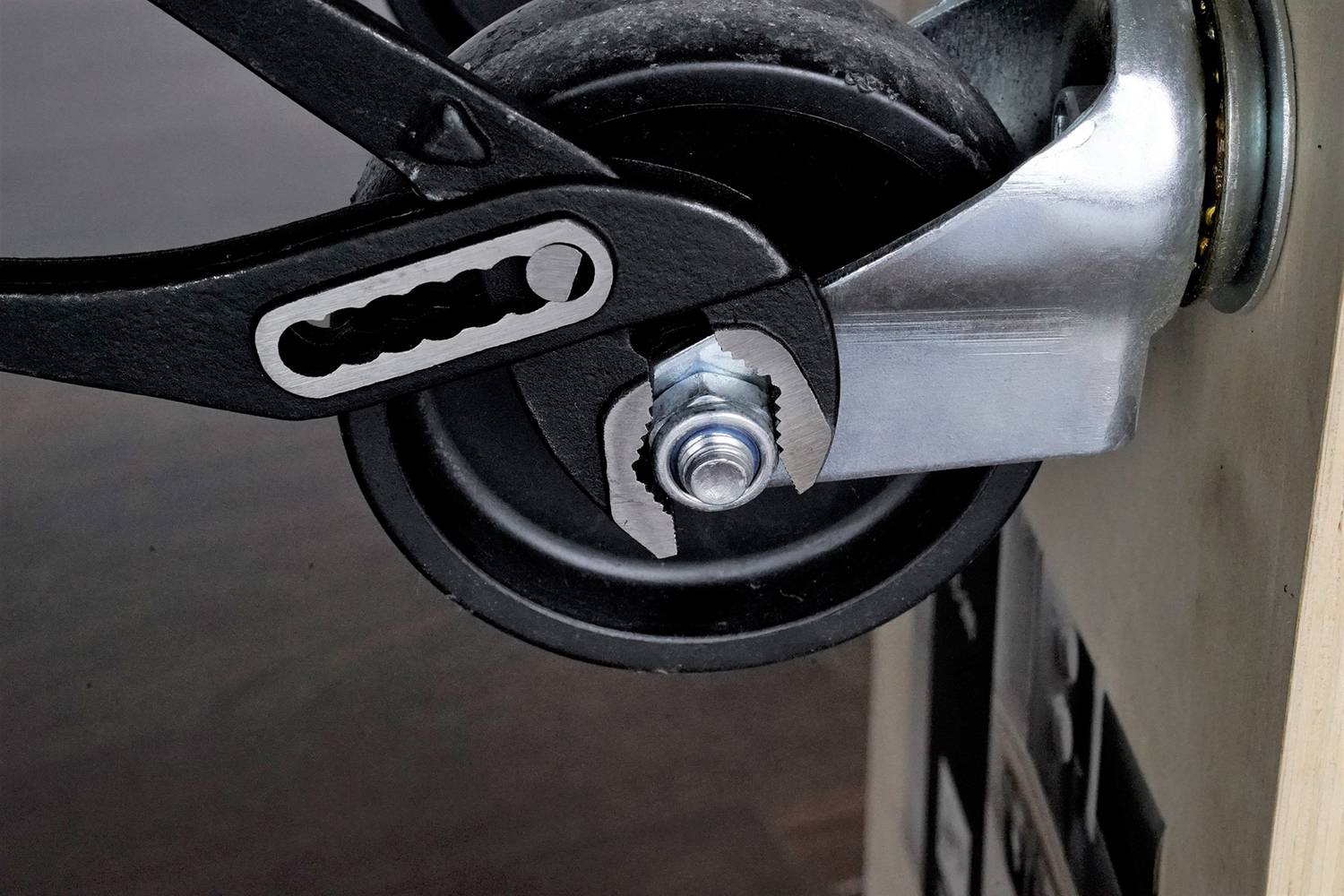 Ein Schraubenschlüssel greift um eine Schraube, die mit einem Rad verbunden ist. Das Rad ist an einem Metallgestell befestigt.