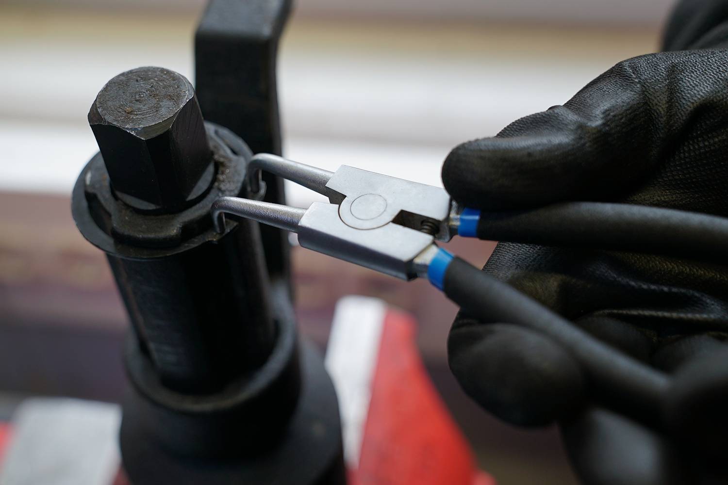 Hand mit scharzen Handschuhen benutzt Zange, um eine Mutter auf einem metallischen Teil zu fixieren oder zu entfernen.