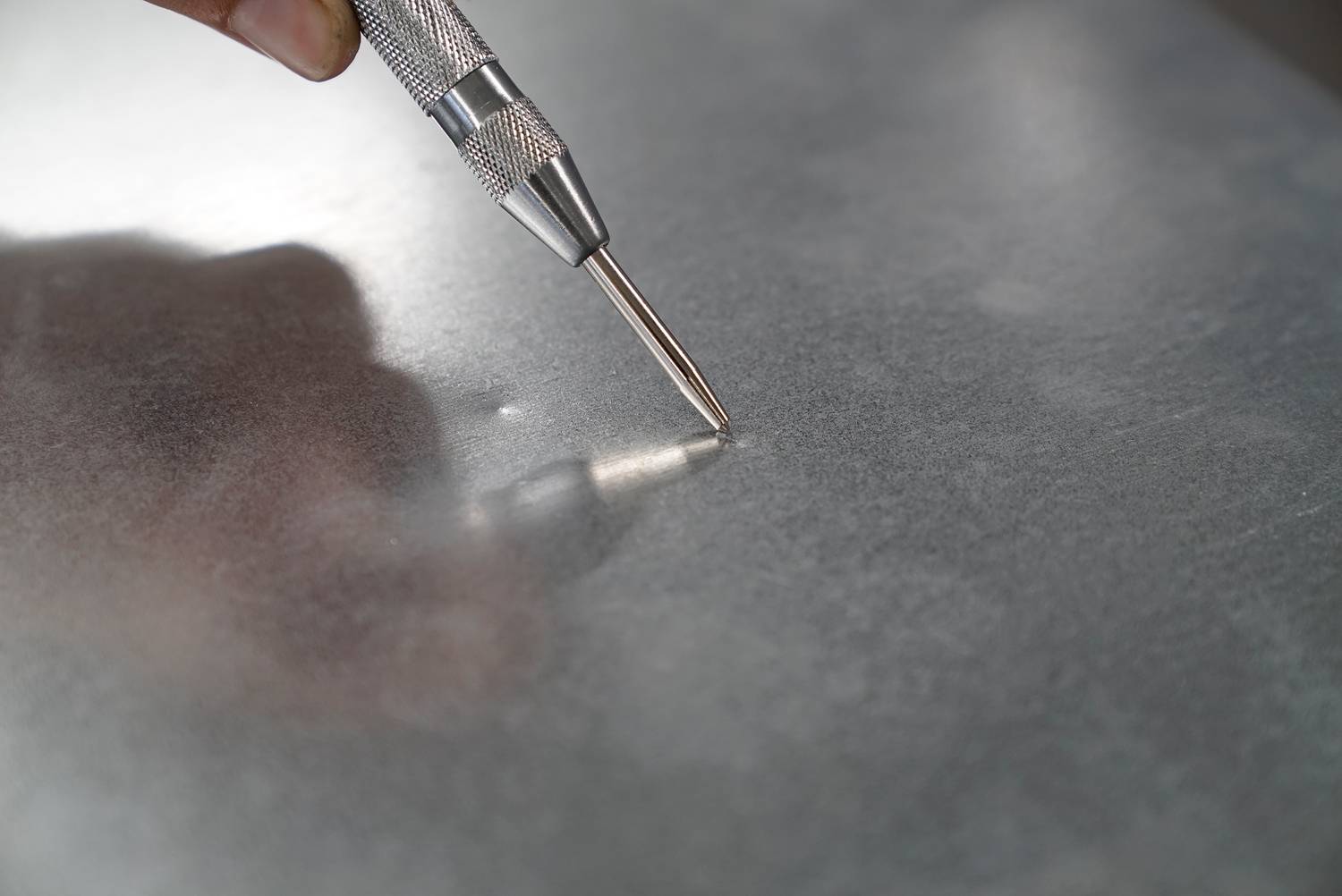 Eine Hand hält einen Metallstift, der auf einer Metallplatte eingesetzt wird, um eine Markierung zu machen.