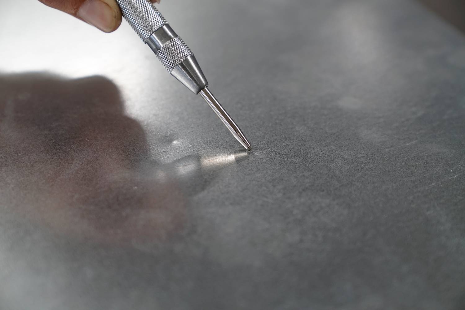 Person hält einen Metallstift auf eine glatte Metalloberfläche, um eine Markierung anzubringen.
