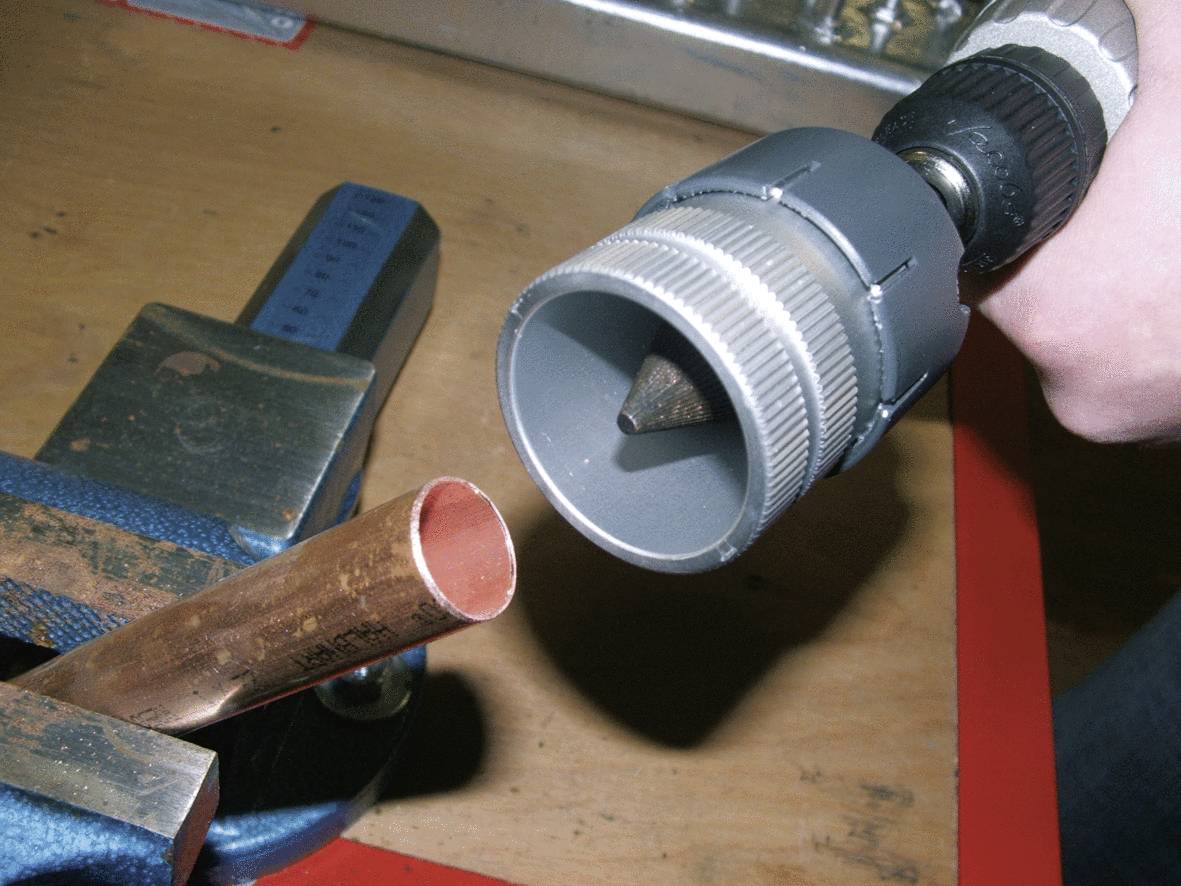Metalrohr in Schraubstock eingespannt. Person hält ein Entgratungswerkzeug.
