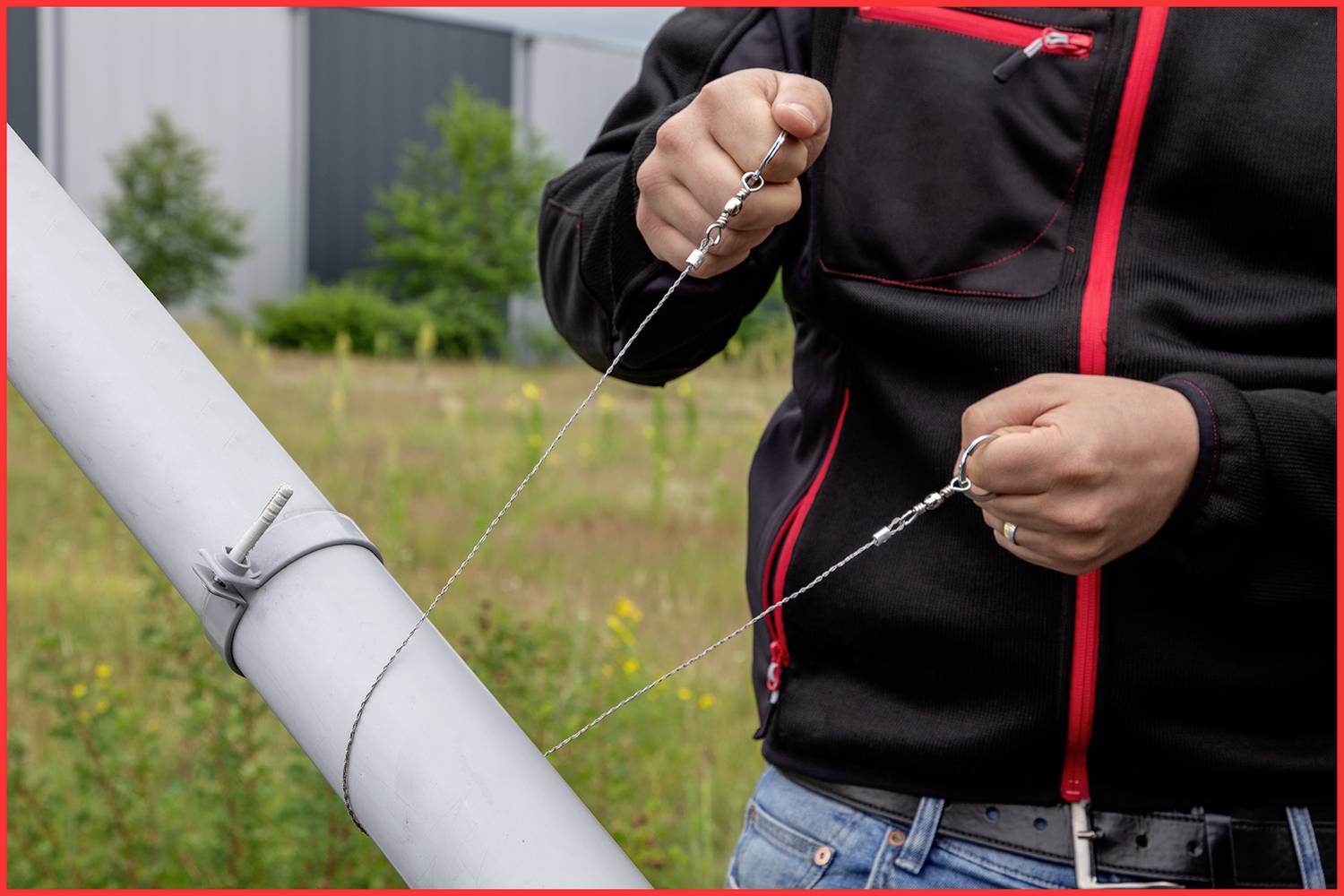 Eine Person spannt ein Drahtseil an einer schrägen Metallstange in einem industriell aussehenden Bereich.