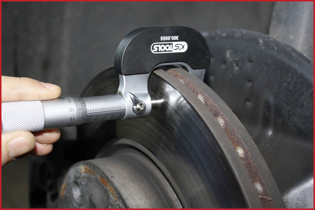 Hand hält ein Mikrometer, misst die Dicke einer Bremsscheibe. Fokus auf präzise Messung zur Bewertung des Verschleißes.