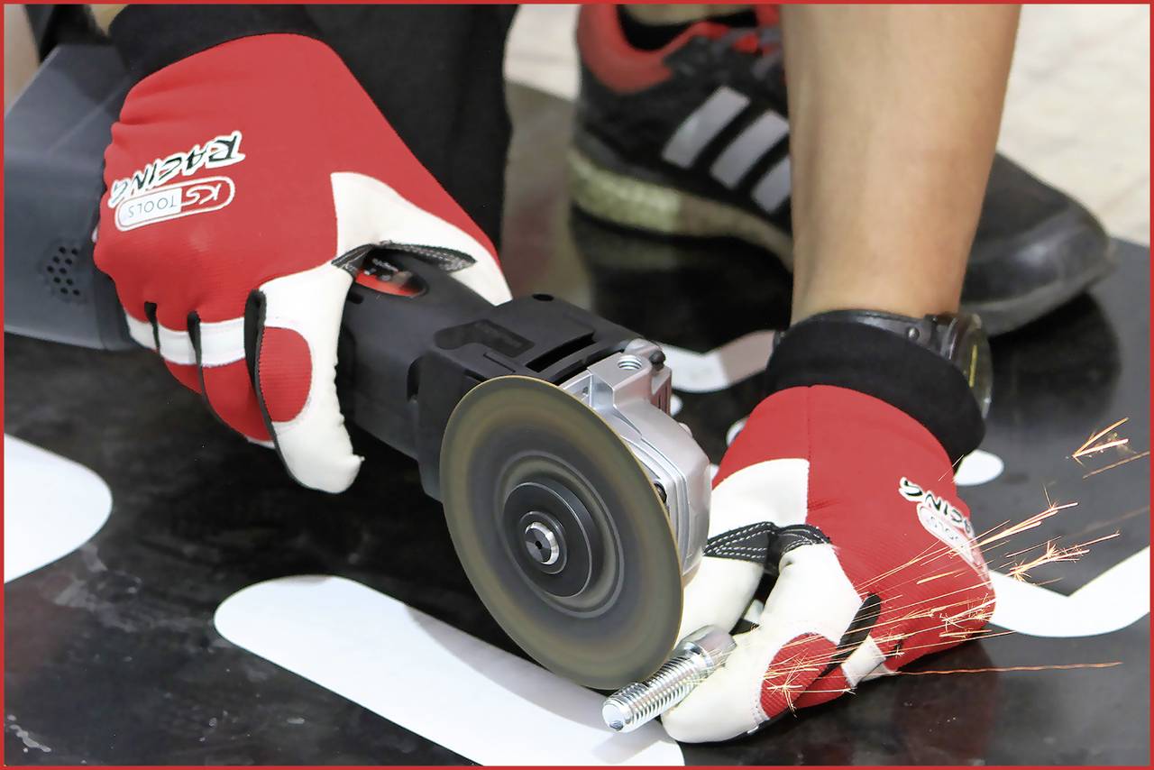 Person trägt Handschuhe und verwendet eine Schleifmaschine, um einen Metallbolzen zu bearbeiten. Funken fliegen vom Kontaktpunkt ab.