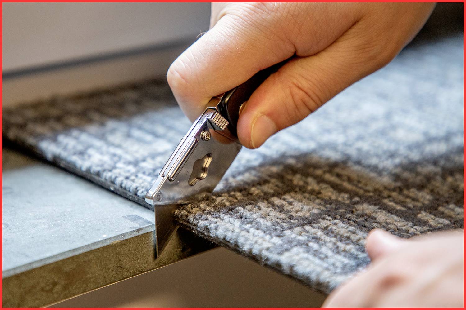 Eine Hand schneidet mit einem Teppichmesser einen grauen Teppichstreifen entlang einer Kante.