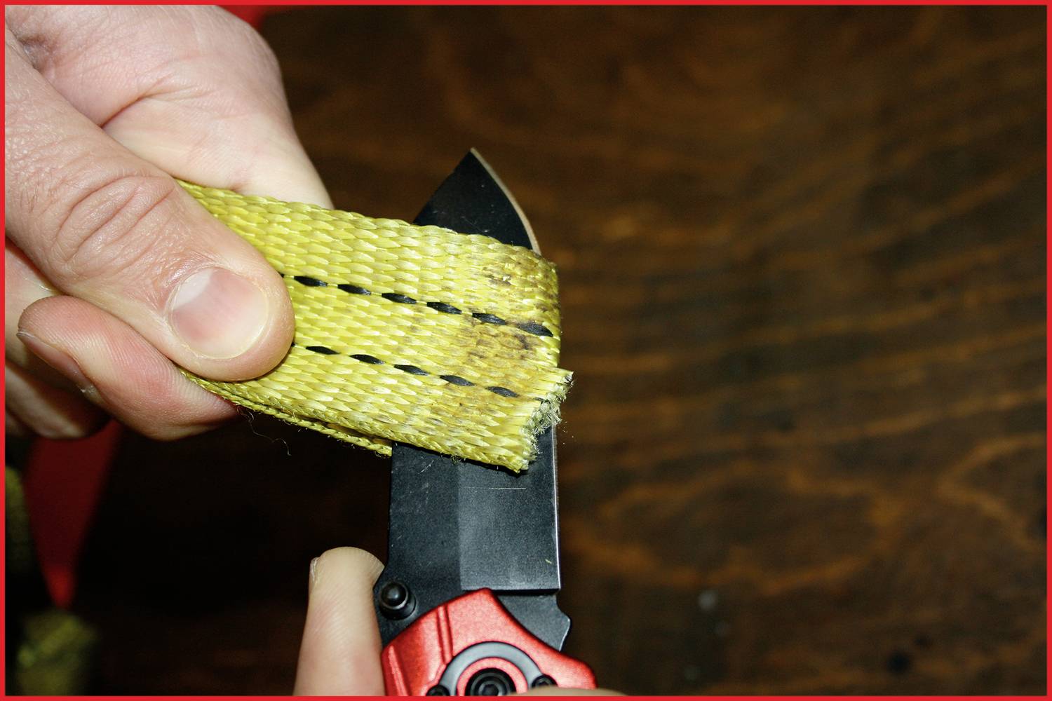 Eine Hand schneidet mit einem roten Taschenmesser ein gelbes Band, das zwei schwarze Linien aufweist. Hintergrund aus dunklem Holz.