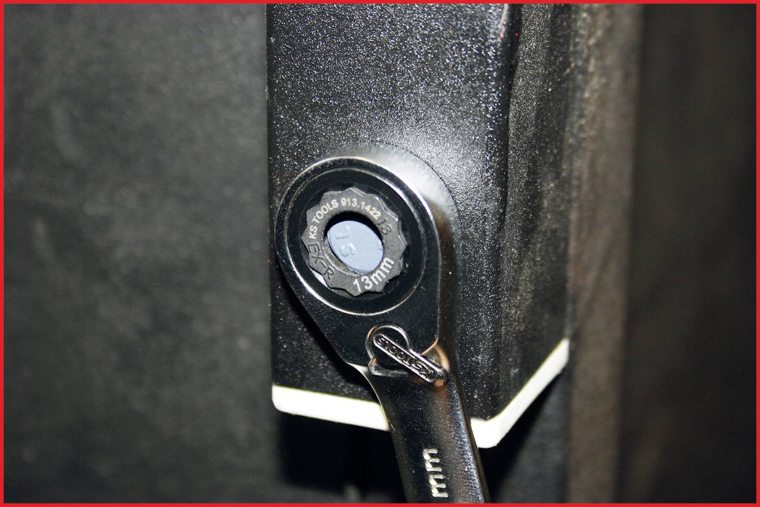 Eine Ratsche befestigt an einer Schraube an einem schwarzen Metallstück. Der Schraubenkopf ist mit der Größe 13 mm markiert.
