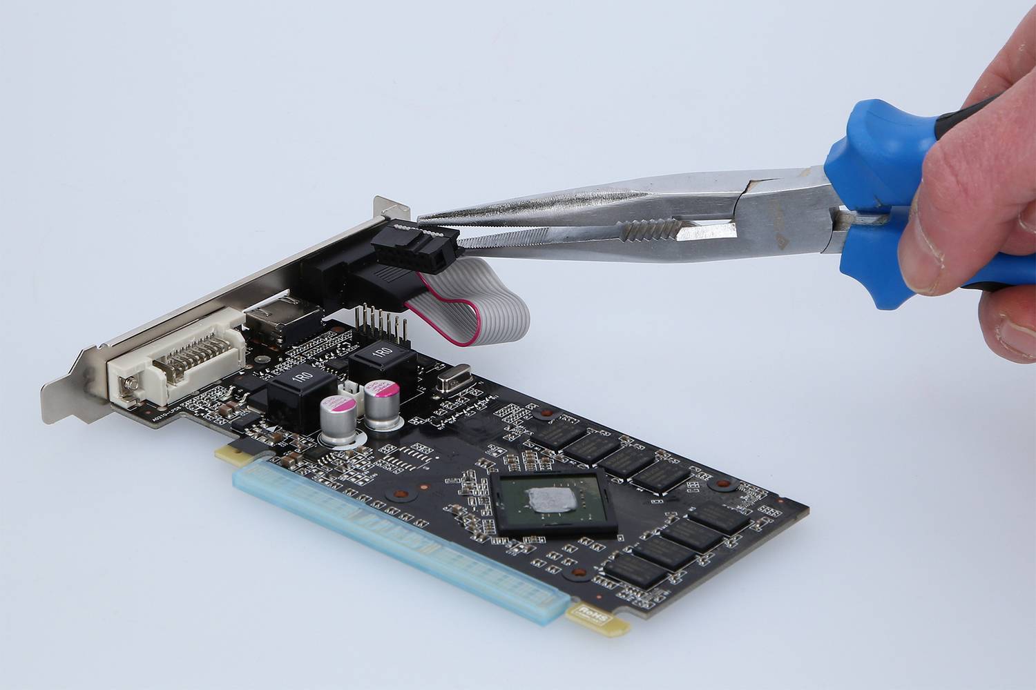 Eine Hand hält eine Zange, die Teile auf einer Computerplatine anpasst. Die Platine hat mehrere Anschlüsse und elektronische Komponenten.