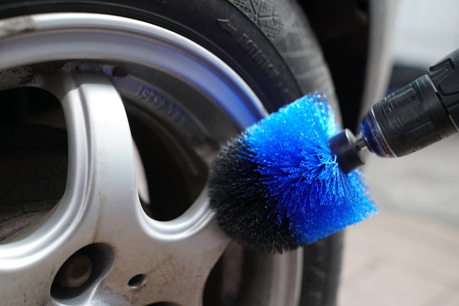 Eine rotierende Bürste mit blauen Borsten reinigt den Felgenrand eines Autoreifens. Der Fokus liegt auf der Sauberkeit der Felge.