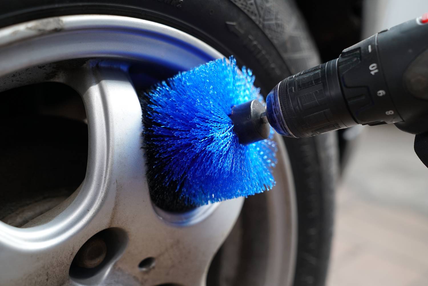 Ein Autoreifen wird mit einer blauen Bürste in einer Bohrmaschine gereinigt; Nahaufnahme zeigt die Reinigungsaktion.