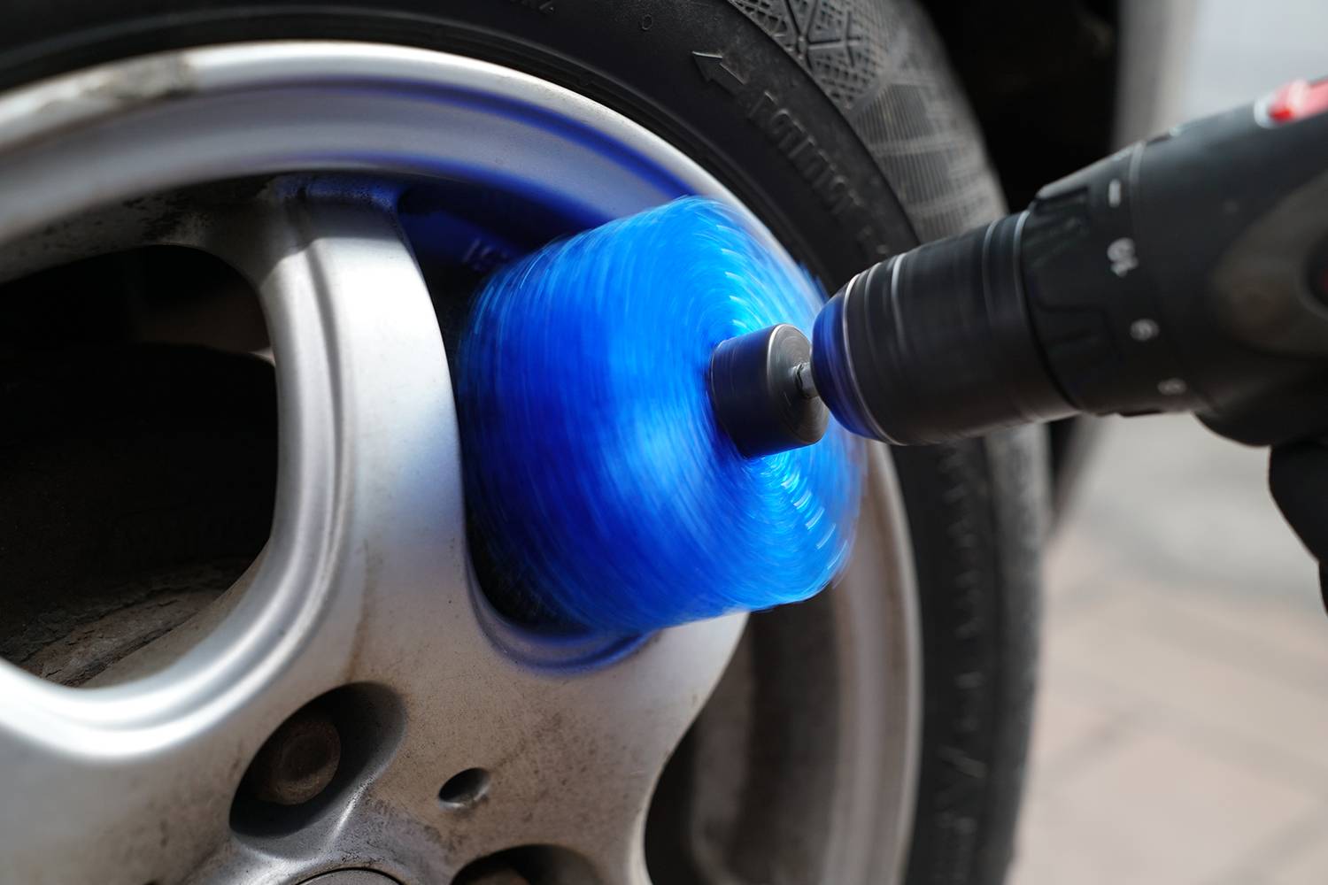 Nahaufnahme eines Autoreifens, der mit einer blauen Bürste an einem Bohrwerkzeug gereinigt wird. Die Felge ist silberfarben.