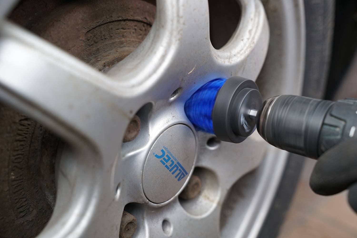 Ein Mechaniker poliert eine Autofelge mit einer blauen Polierscheibe und einer Bohrmaschine.