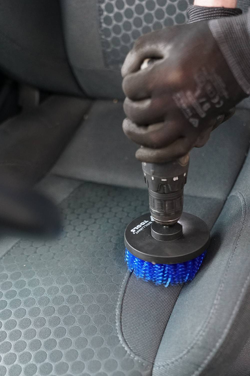 Eine Person reinigt mit einer blauen Bürste den Sitz eines Autos. Die Bürste ist an einem Gerät befestigt.