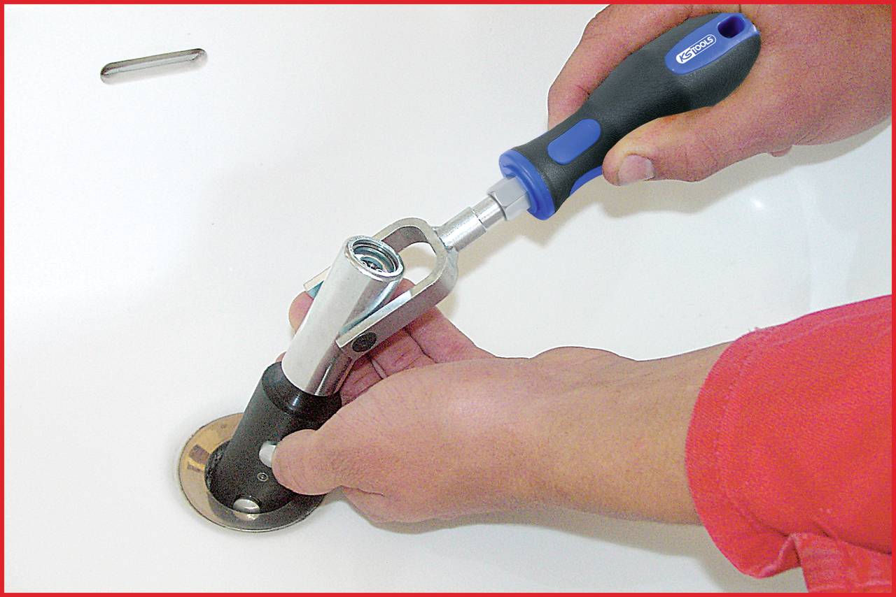 Person repariert einen Abfluss mit einem Werkzeug in einem Badezimmer.