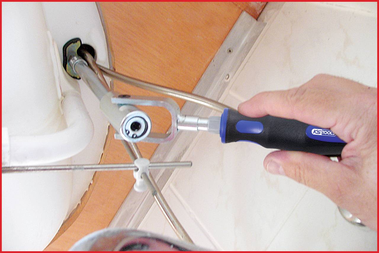 Eine Hand hält ein Werkzeug an einer Rohrverbindung unter einem Waschbecken. Das Werkzeug wird verwendet, um die Verbindung zu lösen.