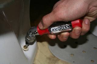 Eine Hand verwendet einen KS Tools Ratschenringmaulschlüssel, um eine Schraube an einem weißen Gegenstand festzuziehen.