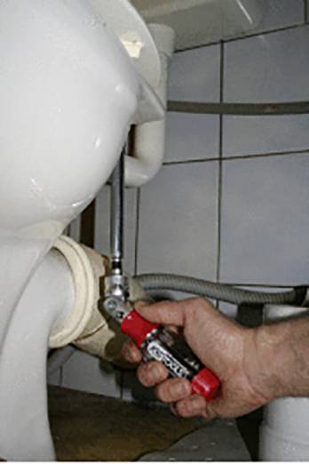 Eine Person zieht mit einem Schraubenschlüssel eine Schraube an der Seite einer Toilette fest, um diese zu sichern oder zu reparieren.