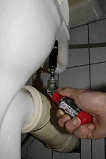 Eine Hand mit einem Schraubenschlüssel zieht an einem Rohr unter einer weißen Toilette an einem Verbindungselement.