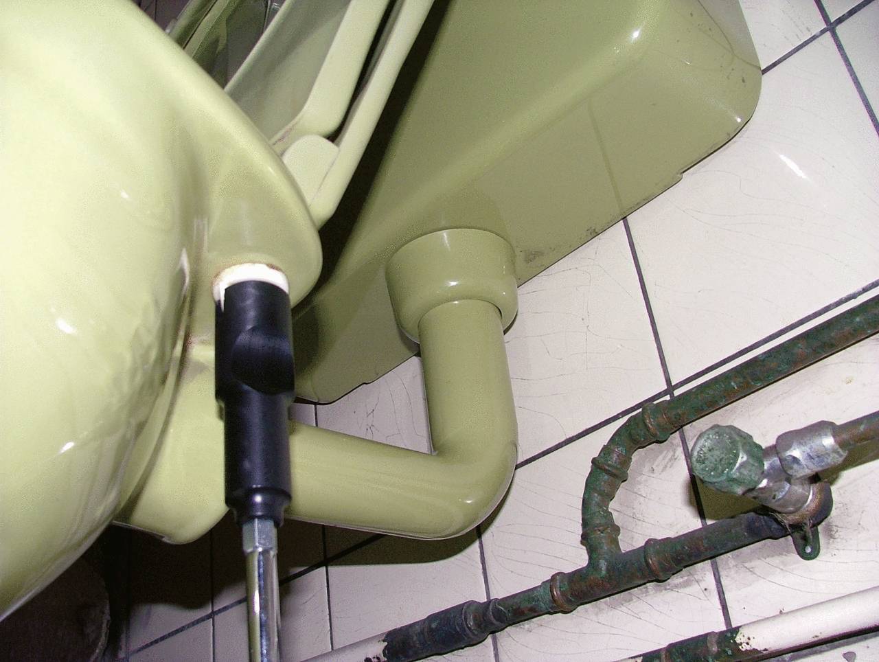 Grünes Waschbecken von unten, zeigt Abflussrohr und angrenzende Leitungen auf Fliesenhintergrund.