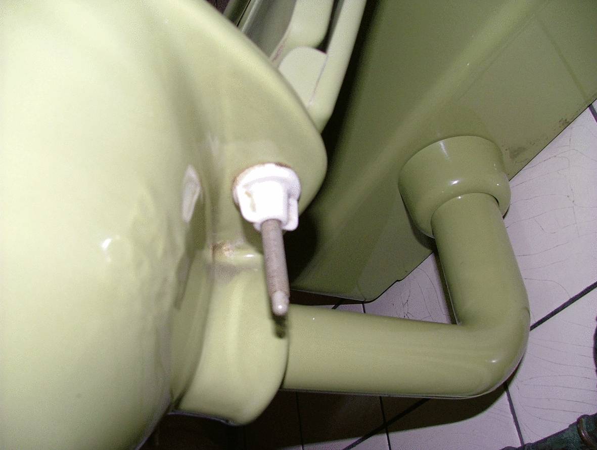 Ein altes, olivgrünes Waschbecken mit sichtbarem Abflussrohr und Wandbefestigung, auf weißen Fliesen im Badezimmer montiert.
